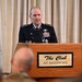 A senior U.S. Air Force officer in dress blue uniform is delivering a speech at a podium at 'The Club at Andrews' (Joint Base Andrews, Maryland). The officer displays four-star rank insignia on his shoulders, along with numerous service ribbons, badges, and decorations on his uniform. An audience is partially visible in the foreground.