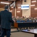 A civilian instructor in a dark suit is presenting a 'Russian Way of War Course' to a room full of military personnel in camouflage uniforms. The setting appears to be a modern military education facility or conference room with tiered seating. The students are seated at long wooden tables and appear attentive to the lecture.