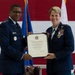 Two United States Air Force officers in dress uniforms are jointly holding a Certificate of Retirement during a formal military retirement ceremony. The certificate is made out to Lieutenant General Rebecca Sonkiss, retired from the United States Air Force on the First day of November, Two Thousand Twenty-Six. The ceremony takes place in front of American and Air Force flags in what appears to be a hangar or large ceremonial hall.