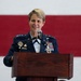 A female U.S. Air Force officer in dress blues is speaking at a wooden podium with a microphone. She is wearing a high-ranking uniform adorned with multiple medals, ribbons, and insignia, with three stars visible on her shoulder indicating the rank of Lieutenant General. An American flag is displayed prominently in the background.