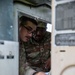 Two U.S. Army soldiers in OCP (Operational Camouflage Pattern) uniforms are examining or working inside what appears to be a military vehicle or equipment compartment. One soldier, identified by a name tape as 'COOPER,' is visible along with a second soldier wearing glasses. They appear to be conducting maintenance, inspection, or training on the equipment.