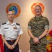 Two military officers pose for a formal photograph in front of institutional insignia. One officer wears a white dress uniform consistent with the Japan Maritime Self-Defense Force, while the other wears U.S. Marine Corps MARPAT camouflage utilities. The setting appears to be an official meeting room at a U.S. Marine Corps Forces Pacific facility.