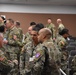 A group of U.S. Army soldiers in OCP (Operational Camouflage Pattern) uniforms are gathered in what appears to be a conference or briefing room. The soldiers are engaged in informal conversations and networking, with several wearing name tags and unit patches visible on their uniforms. The setting suggests a military training event, conference, or professional development gathering.