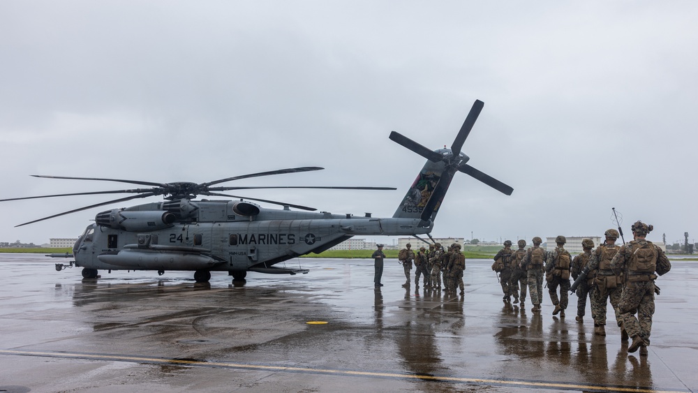 A group of U.S. Marines in full combat gear are boarding or preparing to board a large military helicopter on a wet tarmac during overcast, rainy conditions. The helicopter is clearly marked 'MARINES' with the number '24' and tail number '4539', identifiable as a Sikorsky CH-53E Super Stallion. The scene appears to be a tactical loading operation at a military airfield.