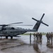 A group of U.S. Marines in full combat gear are boarding or preparing to board a large military helicopter on a wet tarmac during overcast, rainy conditions. The helicopter is clearly marked 'MARINES' with the number '24' and tail number '4539', identifiable as a Sikorsky CH-53E Super Stallion. The scene appears to be a tactical loading operation at a military airfield.