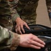Two military personnel in OCP (Operational Camouflage Pattern) uniforms are handling what appears to be a ruggedized military electronic device or portable computing/communications equipment in a protective case. The image is a close-up shot focusing on their hands and the equipment. At least one patch is visible on the upper arm of one soldier.