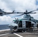 Two U.S. Marines UH-1Y Venom helicopters are operating on what appears to be the flight deck of a naval amphibious assault ship at sea. The foreground helicopter, numbered '63', is on deck with rotors spinning while a crew member stands nearby, and a second helicopter is airborne in the background. The 'MARINES' marking is visible on the fuselage, confirming U.S. Marine Corps ownership.