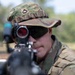 A U.S. Army soldier in Operational Camouflage Pattern (OCP) uniform is aiming a weapon directly toward the camera. The soldier wears a rank insignia patch on their patrol cap consistent with Private First Class (PFC). The image is a close-up shot taken outdoors in a wooded or field training environment.