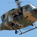 A Sri Lanka Air Force helicopter is conducting a medical evacuation (MEDEVAC) or search-and-rescue operation. Personnel are hoisting a casualty on a stretcher/litter via rope while a crew member leans out of the open door to assist. This appears to be either a live rescue operation or a training exercise demonstration.