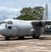 A Sri Lanka Air Force C-130 Hercules transport aircraft (serial number 280) is parked on a concrete apron at a military airbase. A uniformed personnel member stands in front of the aircraft, appearing to photograph or observe it. The propellers are spinning, indicating the engines are running or have recently been started.