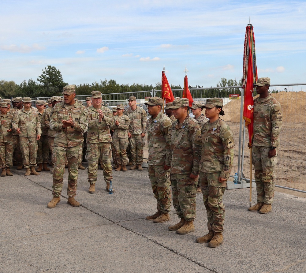 A group of U.S. Army soldiers in OCP (Operational Camouflage Pattern) uniforms are assembled in formation during what appears to be a military ceremony or award presentation. A senior officer appears to be addressing or presenting awards to several soldiers standing at attention in the foreground. Military guidons and unit colors are visible, suggesting a formal unit ceremony conducted outdoors.