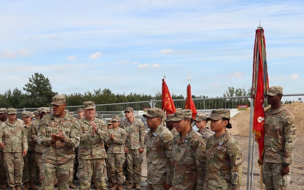 A group of U.S. Army soldiers in OCP (Operational Camouflage Pattern) uniforms are assembled in formation during what appears to be a military ceremony or award presentation. A senior officer appears to be addressing or presenting awards to several soldiers standing at attention in the foreground. Military guidons and unit colors are visible, suggesting a formal unit ceremony conducted outdoors.