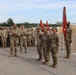 A group of U.S. Army soldiers in OCP (Operational Camouflage Pattern) uniforms are assembled in formation during what appears to be a military ceremony or award presentation. A senior officer appears to be addressing or presenting awards to several soldiers standing at attention in the foreground. Military guidons and unit colors are visible, suggesting a formal unit ceremony conducted outdoors.