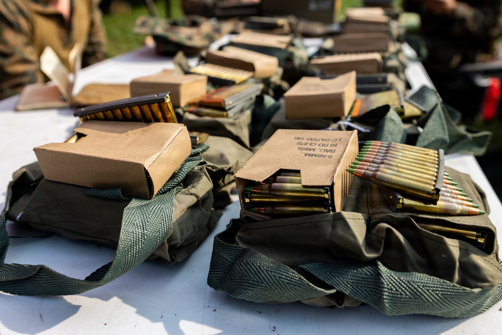 The image shows multiple military ammunition pouches and cardboard boxes laid out on a white table. The boxes are labeled '5.56MM Ball M855 10 RD Clips' and contain stripper clips loaded with 5.56×45mm NATO cartridges. This appears to be an ammunition distribution or pre-range preparation setup in a military or training environment.