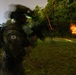A South Korean military soldier is photographed during a nighttime live-fire training exercise. The image shows motion blur from a long exposure, capturing tracer rounds and an explosion or target detonation in the background. The soldier is equipped with full tactical gear including night vision equipment and is actively firing a weapon.