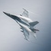 A twin-engine fighter jet, identifiable as an F/A-18 Super Hornet, is captured in a high-speed, banked maneuver against an overcast gray sky. Dramatic vapor condensation trails (Prandtl-Glauert condensation) are visibly streaming across the fuselage, wings, and leading edges due to rapid pressure changes at high speed. The aircraft bears the number '104' on its nose and appears to be in a steep climbing or rolling attitude.