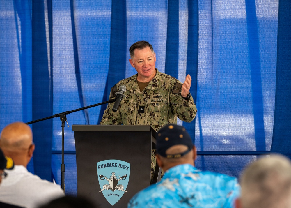 A U.S. Navy officer with the name tag 'ZERR' and a single star insignia (Rear Admiral Lower Half/Brigadier General equivalent) is speaking at a podium bearing the Surface Navy Association logo. The officer is wearing Navy Working Uniform (NWU) digital camouflage and is gesturing with one hand while addressing an audience. The event appears to be a Surface Navy Association gathering or symposium.
