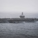 A large US Navy aircraft carrier is underway at sea under overcast, hazy conditions. The hull number '73' is clearly visible on the island superstructure, identifying it as the USS George Washington (CVN-73), a Nimitz-class nuclear-powered carrier. Multiple fixed-wing aircraft are visible parked on the flight deck.