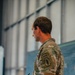 A U.S. Army soldier in Operational Camouflage Pattern (OCP) uniform is photographed from behind/side profile, holding a notebook and pen in what appears to be an indoor briefing or planning environment. The soldier displays multiple qualification tabs on the left shoulder sleeve, indicating an elite special operations background. A map or tactical display board is partially visible in the background.