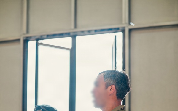 Two military personnel are standing indoors, appearing to attend a briefing or training session. The foreground figure wears US Army MultiCam (OCP) uniform with multiple qualification tabs, while the background figure wears a Philippine Armed Forces woodland camouflage uniform with a 'TERP' (interpreter) patch. This appears to be a joint US-Philippine military exercise or training event.