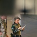 Two military personnel are visible in what appears to be an indoor operations or briefing area. The central figure, wearing Indonesian Armed Forces (TNI) camouflage uniform with an 'INDONESIA' name tape and flag patch, is reviewing a document or map. A second soldier in MultiCam/OCP pattern uniform, likely US military, is partially visible on the left.