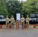 Four military personnel in Australian Army camouflage uniforms and distinctive wide-brimmed slouch hats are posing in front of a Japanese military museum sign reading '第七師団史料館' (7th Division Historical Museum). They are flanked by two static display tanks on a gravel outdoor area. The setting appears to be a Japanese Ground Self-Defense Force base, likely in Hokkaido, Japan.