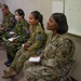 Military personnel from multiple nations are seated in a classroom or briefing room setting, appearing to attend a joint training or coordination session. At least three distinct national uniforms are visible, including Japanese Self-Defense Force, Australian Defence Force, and United States Army. Several individuals are holding notebooks, suggesting active note-taking during a presentation or lecture.