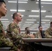Military personnel from what appears to be the U.S. Army and Japanese Ground Self-Defense Force are seated together in a modern briefing or conference room. The soldiers are attentively facing forward, suggesting they are participating in a joint training session, briefing, or educational event. The setting indicates a formal multinational military cooperation or exchange program.