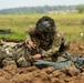 A soldier wearing multicam camouflage uniform and a ghillie-style face covering is kneeling on disturbed dirt terrain, handling equipment after what appears to be a parachute landing. The soldier has a unit patch visible on the left shoulder, identifiable as the 11th Airborne Division patch. A military rucksack is positioned to the left, and parachute rigging or canopy material is spread to the right.