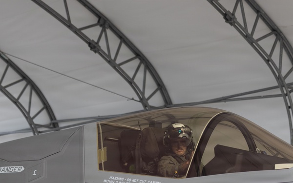 A military pilot is seated in the cockpit of an F-35 Lightning II fighter jet, parked inside a temporary fabric hangar structure. The aircraft bears the name 'LT C.S. O'REILLY' with the callsign 'SPLASH' and the aircraft number '06', along with standard U.S. military markings. The pilot is wearing a full flight helmet and appears to be conducting pre-flight or post-flight procedures.