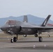 A U.S. Marine Corps F-35B Lightning II stealth fighter jet is taxiing on an airfield tarmac. The aircraft bears the markings of VMFA-533 squadron with tail code '00' and a distinctive shark/ghost tail art. A second aircraft is partially visible in the background to the right.