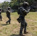 A group of soldiers wearing South Korean military uniforms and tactical gear are conducting a live-fire or combat training exercise on an outdoor range. The soldiers are advancing in a line formation while aiming their rifles toward targets visible in the background. The setting appears to be a grassy field with forested hills in the background.