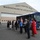 104th Fighter Wing hosts Springfield Chamber of Commerce Breakfast A group of civilians is gathered in a parking area outside the 104th Fighter Wing, Massachusetts Air National Guard hangar facility. They appear to be on an organized visit or tour, standing in a loose line alongside a blue bus. The setting suggests an official community outreach, employer support, or civic leader tour event.
