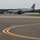 104th Fighter Wing Celebrates Flight Surgeon's Fifteen Years of Service with Fini Flight A U.S. Air Force KC-135 Stratotanker aircraft with tail code 'AK' and serial number 0332 is taxiing on an airfield tarmac. The aircraft bears Alaska Air National Guard markings, identifiable by the polar bear emblem on the tail fin. The setting appears to be a regional or military airfield surrounded by forested hills under overcast skies.