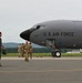 A U.S. Air Force aircraft, marked with tail number 0332, is parked on a tarmac at what appears to be a military airfield. Several personnel in military flight suits and camouflage uniforms are gathered near the nose of the aircraft. The setting appears to be a routine ground operation, possibly an arrival or pre-flight inspection.