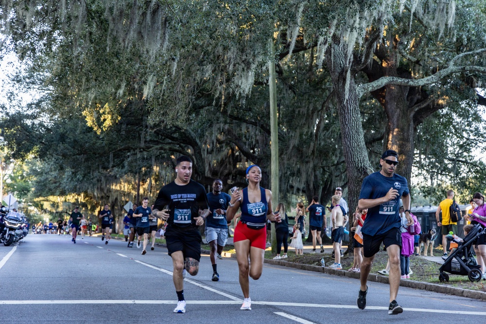 A road race event is taking place on a tree-lined street canopied with large live oak trees draped in Spanish moss, suggesting a Southern U.S. location such as Georgia or Florida. Multiple runners wearing bib number 911 are prominently visible in the foreground, with spectators lining the sidewalk. The lighting suggests early morning or late afternoon conditions.