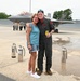 A military pilot in a flight suit poses with a woman on an aircraft tarmac in front of an F-35 fighter jet. The pilot has his arm around the woman and is holding a Monster Energy drink. The setting appears to be a military air base, likely during a post-flight celebration or reunion.