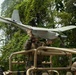 A military service member in camouflage uniform is handling a fixed-wing unmanned aerial vehicle (UAV/drone) while standing on or beside a tan/desert-colored military vehicle. The setting appears to be a tropical or jungle environment based on the dense green foliage in the background. The service member appears to be preparing the UAV for launch or recovering it after a mission.