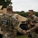 Three U.S. Army National Guard soldiers are gathered near a tan military HMMWV (Humvee) in an outdoor field setting. The soldier facing away from the camera, identified by name tape as 'PEREZ,' is shaking hands with another soldier while a third looks on smiling. The scene appears to be a friendly greeting or recognition moment during a field exercise or operation.
