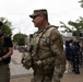 The image shows an FBI agent and a U.S. Army soldier standing together in what appears to be a public outdoor plaza or community event. Both are wearing tactical gear and sunglasses, and appear to be engaged in a friendly conversation. In the background, a group of civilians can be seen gathered near tables, suggesting a community outreach or public safety event.