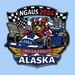 This is a colorful commemorative pin or patch design for NGAUS 2026 in Indianapolis, representing the Alaska delegation. It features a cartoon bear mascot wearing a racing helmet driving an IndyCar decorated with Alaska state flag imagery. The design combines Indianapolis Motor Speedway racing themes with Alaskan symbols including mountains, stars, and the number 49 (Alaska's statehood number).