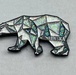 The image shows a decorative souvenir magnet or pin in the shape of a polar bear with a geometric, low-poly design. The bear's body is filled with holographic glitter segments separated by black outlines, creating a mosaic-like appearance. The word 'ALASKA' is embossed in silver lettering on the bear's body.