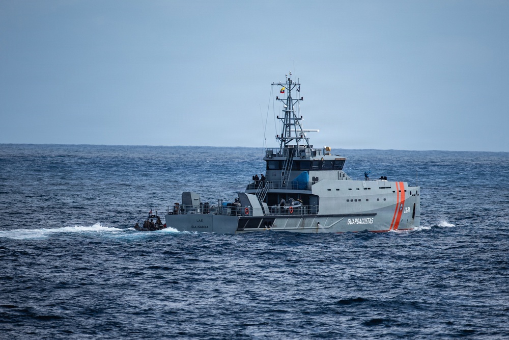 A Guardacostas (Coast Guard) patrol vessel named 'Isla Isabela' is operating at sea, identifiable by its white hull with orange diagonal stripes and hull number. A smaller vessel or intercepted boat appears to be secured or towed at the stern of the patrol ship. The scene suggests a maritime law enforcement or search-and-rescue operation in open ocean conditions.