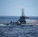A Guardacostas (Coast Guard) patrol vessel named 'Isla Isabela' is operating at sea, identifiable by its white hull with orange diagonal stripes and hull number. A smaller vessel or intercepted boat appears to be secured or towed at the stern of the patrol ship. The scene suggests a maritime law enforcement or search-and-rescue operation in open ocean conditions.
