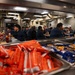 The image shows a military mess hall (galley) aboard USS Mason DDG-87, a U.S. Navy destroyer, with numerous sailors in navy blue uniforms eating a meal. The foreground features serving trays filled with packaged snacks including red and blue wrapped items. A sign reading 'USS MASON DDG 87' and another reading 'WHY WE SERVE' are visible in the background.