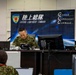 The image shows a Japan Ground Self-Defense Force (JGSDF) command center operation, with personnel seated at workstations beneath a banner reading '陸上総隊 Ground Component Command' (GCC). Two uniformed officers in camouflage uniforms are prominently visible at a command desk, with name placards indicating their roles as Commander (司令官) and Chief of Staff (幕僚長). The setting appears to be a formal military command and control exercise or operational briefing.