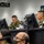 Military personnel in camouflage uniforms are working at computer workstations in what appears to be a command and control center. A banner in the background displays Japanese text '陸上総隊' (Ground Component Command) along with an English translation, indicating this is a Japan Ground Self-Defense Force facility. Multiple monitors and communication equipment are visible throughout the room.