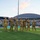 Seven military personnel in Army Combat Uniforms (ACU/OCP camouflage) are standing on a football field during what appears to be a re-enlistment or oath ceremony, with several raising their right hands. The event is taking place at a stadium in Hawaii, identifiable by the distinctive dome structure of the Stan Sheriff Center and sponsor banners including 'Outrigger' and 'Hawaiian Ford.' The stadium is filled with spectators in the background during what appears to be an evening game.