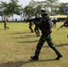 The image shows military personnel in mixed uniforms conducting what appears to be a joint training exercise on an open grass field. Soldiers wearing Indonesian TNI (Tentara Nasional Indonesia) camouflage and others in tan/MultiCam uniforms are moving tactically with rifles. The motion blur in the image suggests dynamic movement during the exercise.