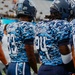 Old Dominion University (ODU) football players are shown from behind wearing special blue digital camouflage uniforms, likely for a military appreciation game. The jerseys display 'LTC SHAH' on the back instead of player names, suggesting a tribute to a military figure. Players wearing numbers 42, 83, 24, and 87 are visible standing on the sideline.